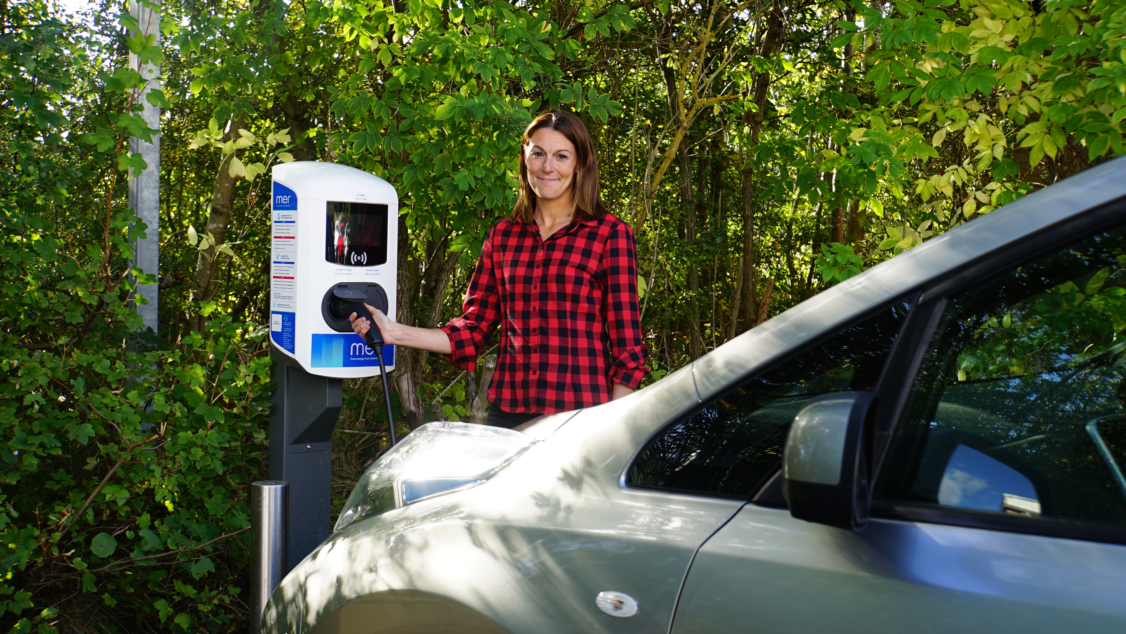Woman plugs in a charger for an electric car