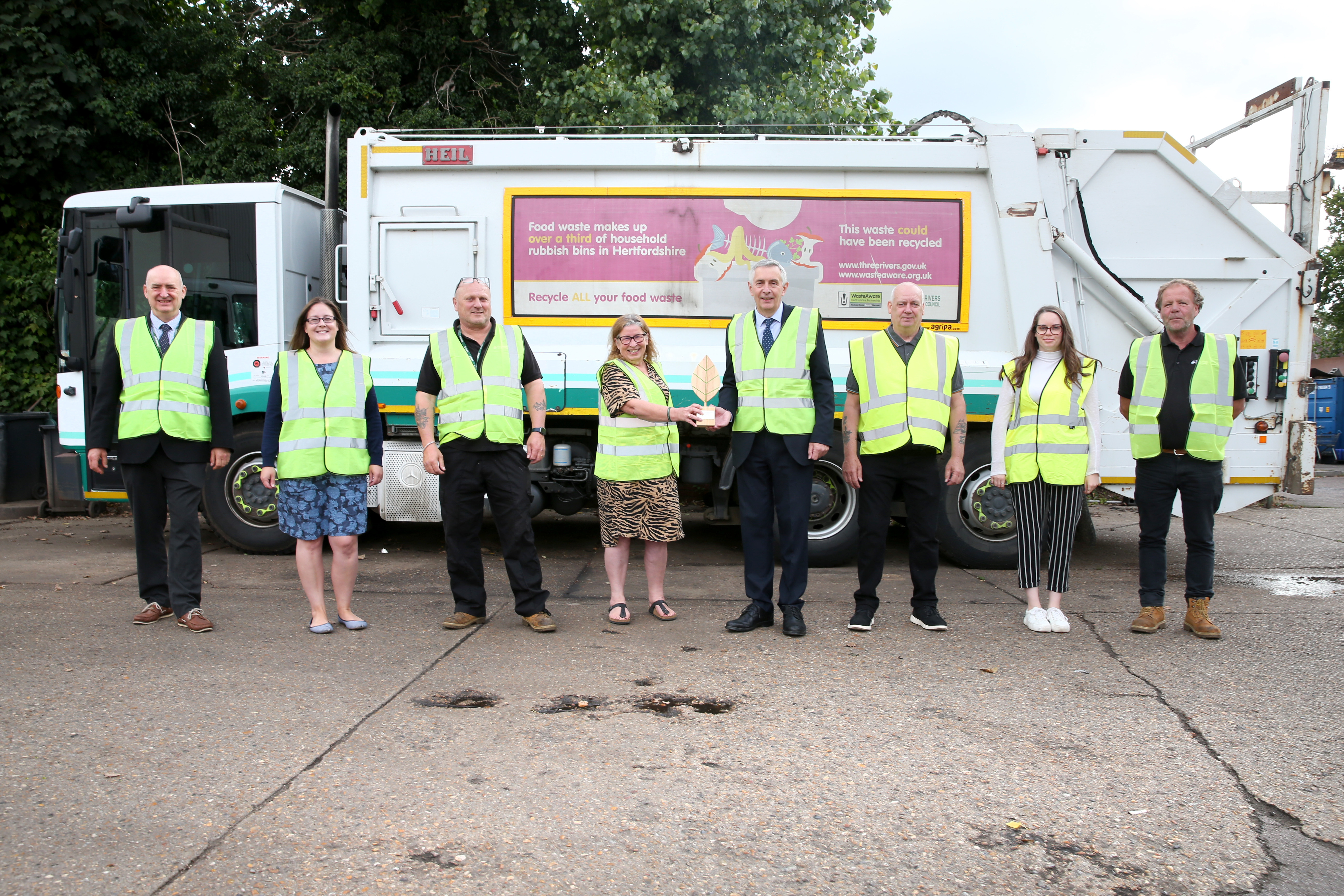 Council members stand in front of a recycling lorry, holding an award