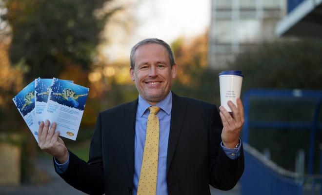 Man holds up leaflets and a biodegradable coffee cup.