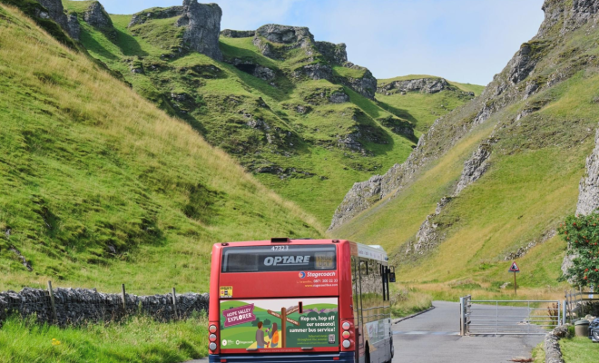 The back view of a red bus driving into a green valley
